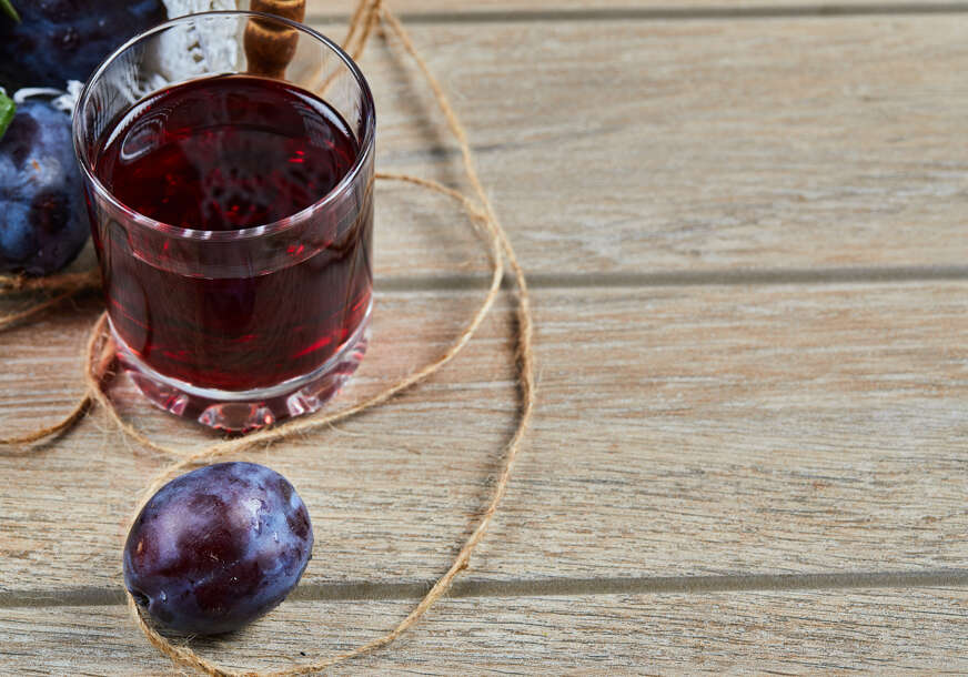 A glass of juice and garden plums in a wooden table